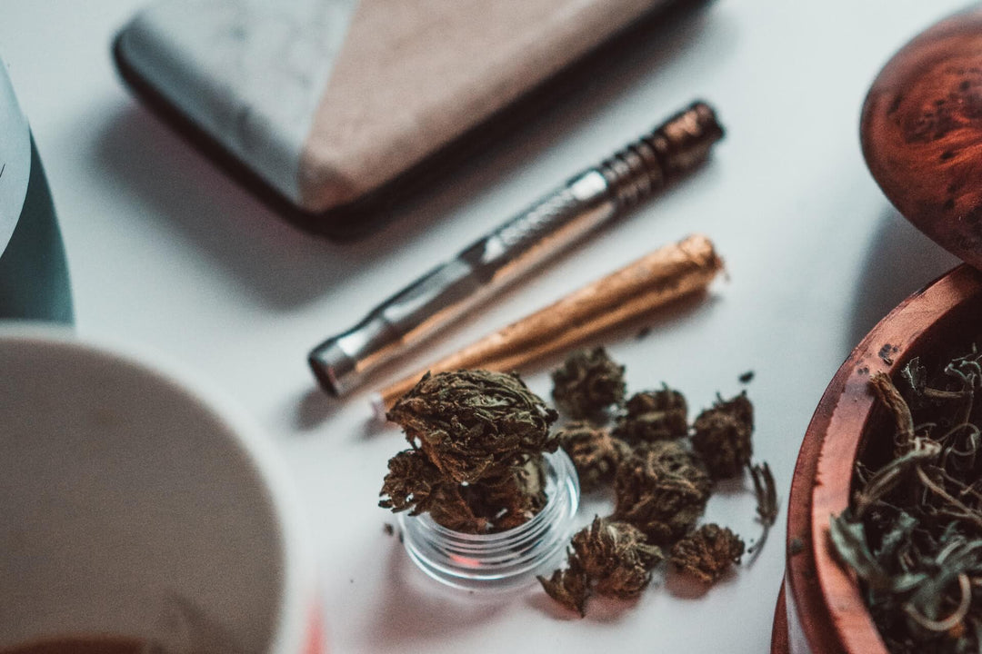 Close-up of hemp buds with grinder, metal pipe, and rolling paper on a table