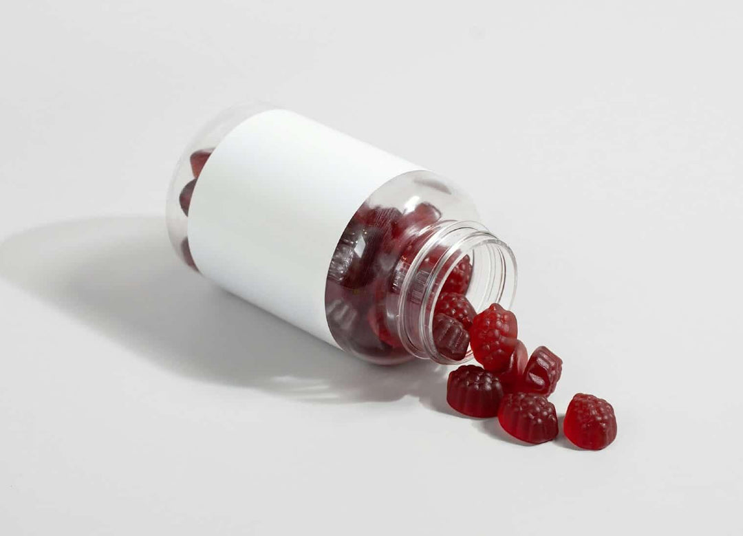 Red mushroom-shaped gummies spilling from clear bottle on white background