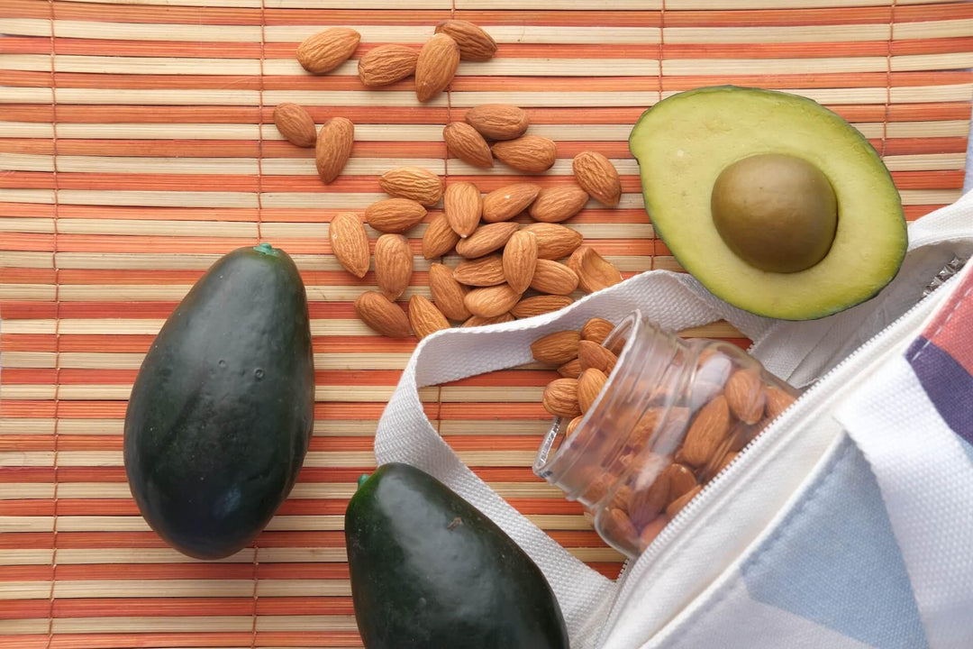 Avocado and almonds on bamboo mat with a white bag and jar