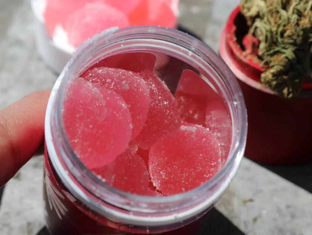 Close-up of pink cannabis gummies in a jar with cannabis bud in background