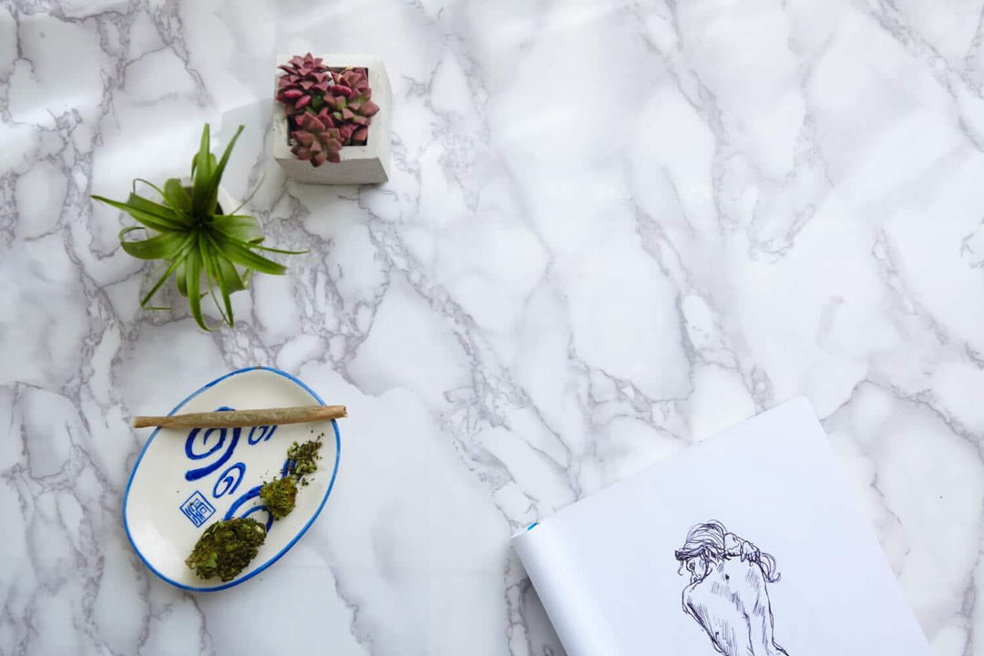 THCA flower buds and joint on decorative plate with plants and sketchbook on marble table