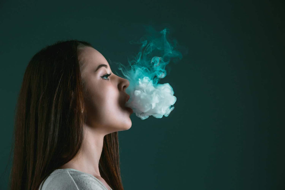 Woman vaping cannabis, blowing thick vapor against dark background