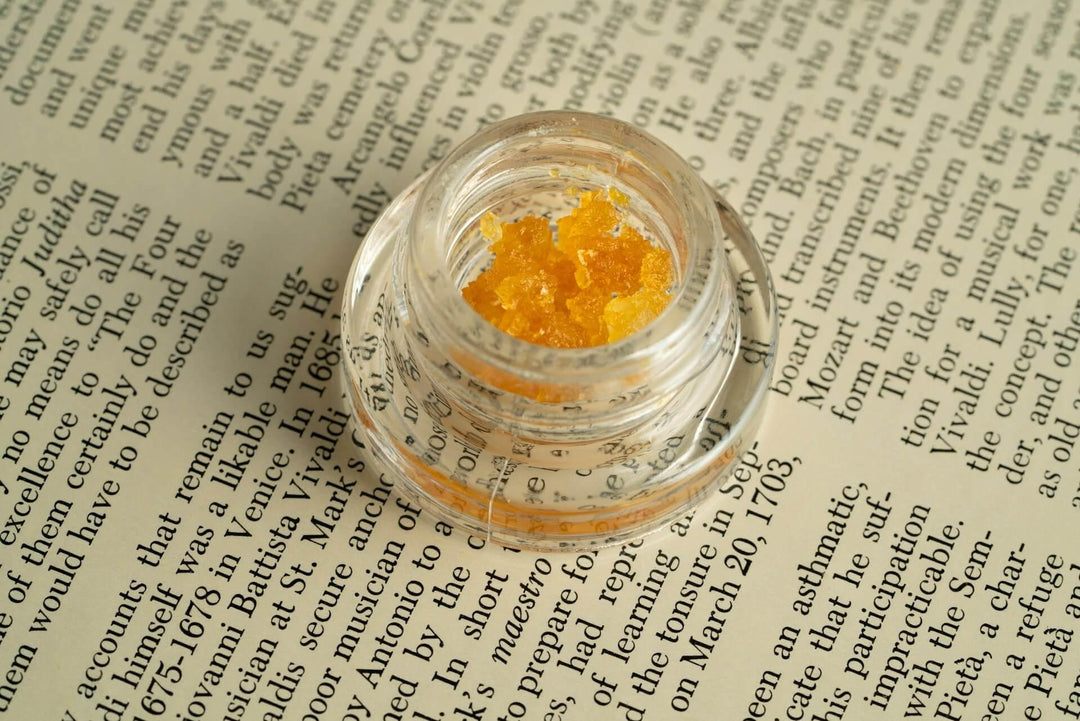 Clear jar of golden cannabis concentrate on an open book page