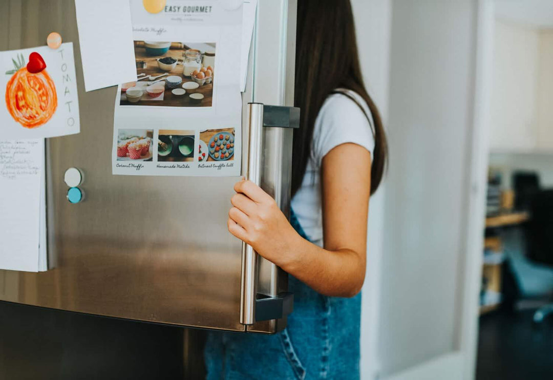 Woman opening stainless steel refrigerator with magnets, recipes, and drawing on door