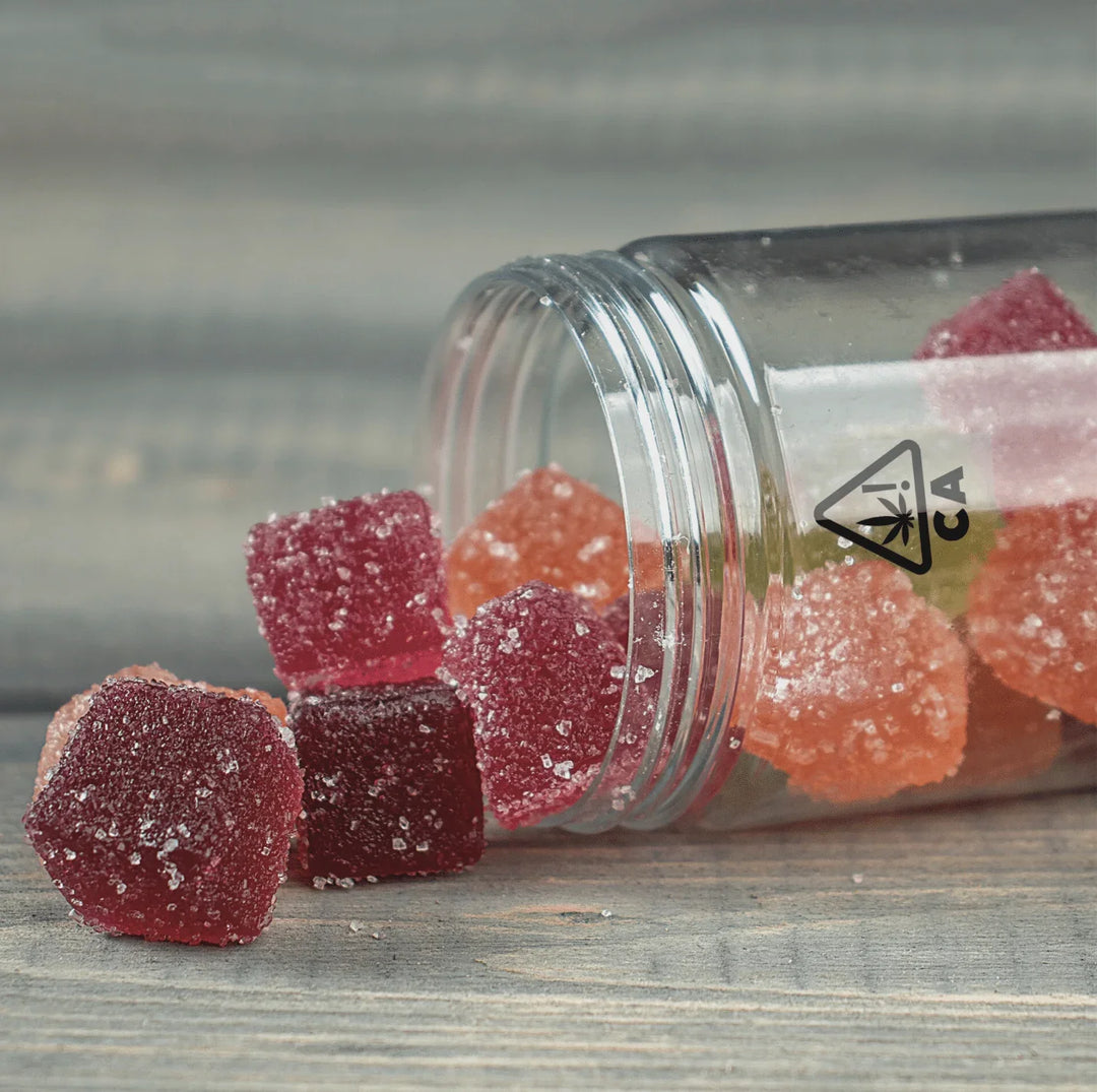 Assorted cannabis gummies spilling from labeled jar on wooden surface