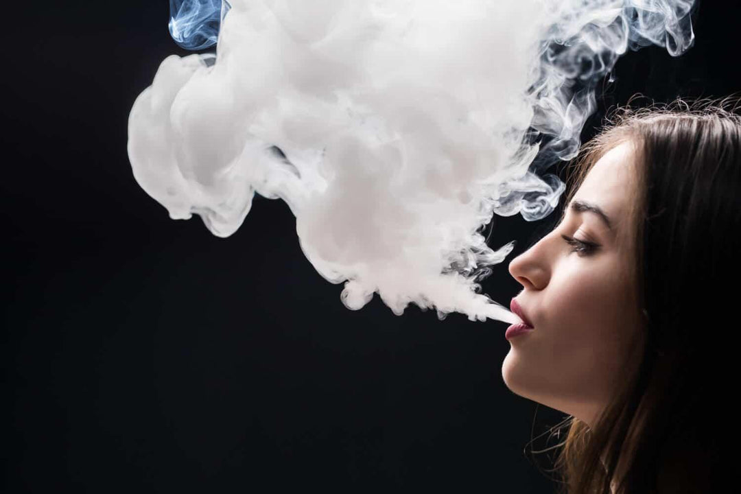 Woman exhaling dense vape cloud against a dark background, vaping concept