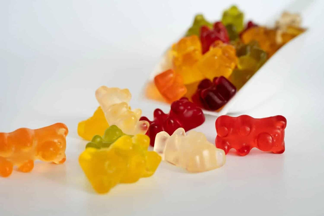Colorful Delta-9 gummy bears scattered on white background near a white scoop