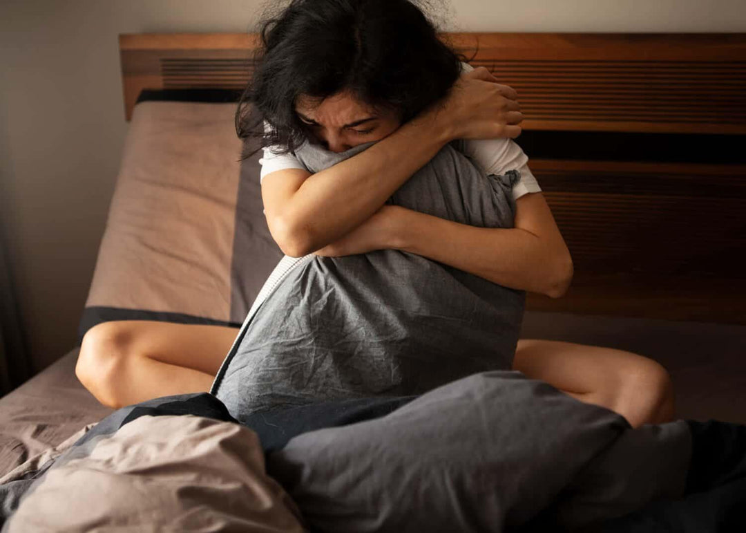 Woman sitting on bed hugging pillow, looking stressed and anxious in bedroom